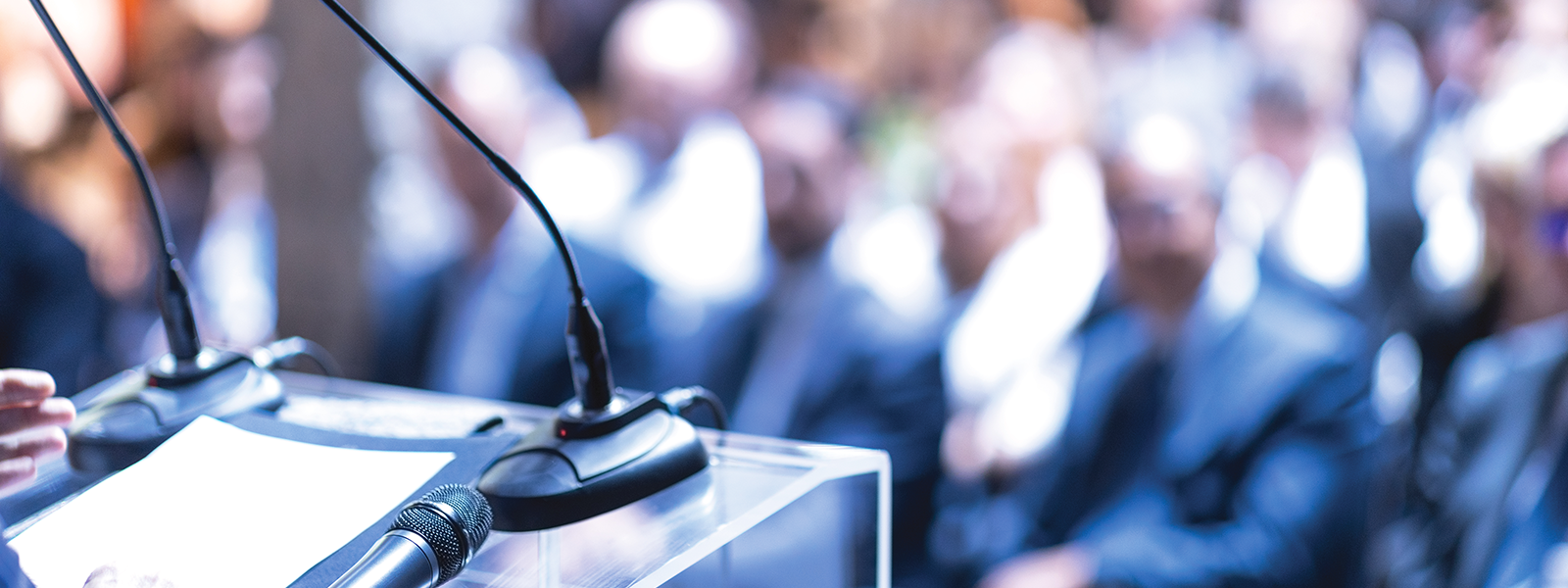 Podium and microphone at a conference with blurred audience in background banner image