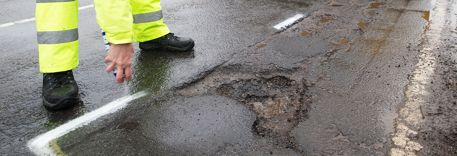 Roadworker sprays road to mark pothole that needs repairing banner image