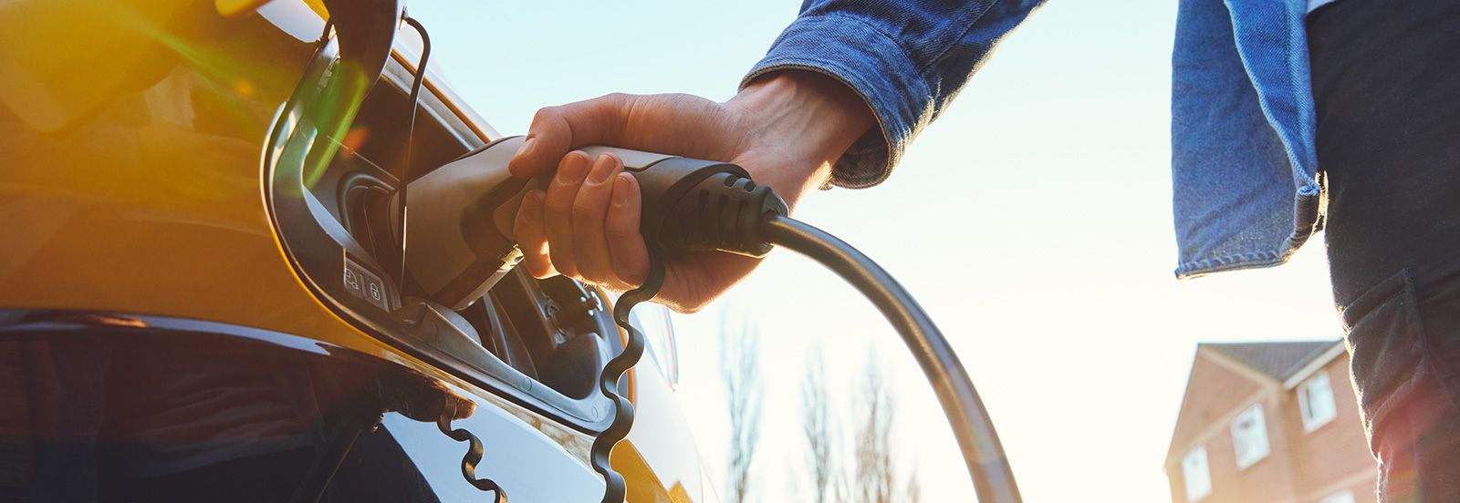 A man plugs a charger into his electric car banner image