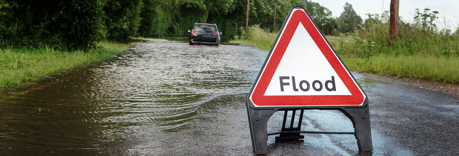 Flooded road with flood warning sign banner image