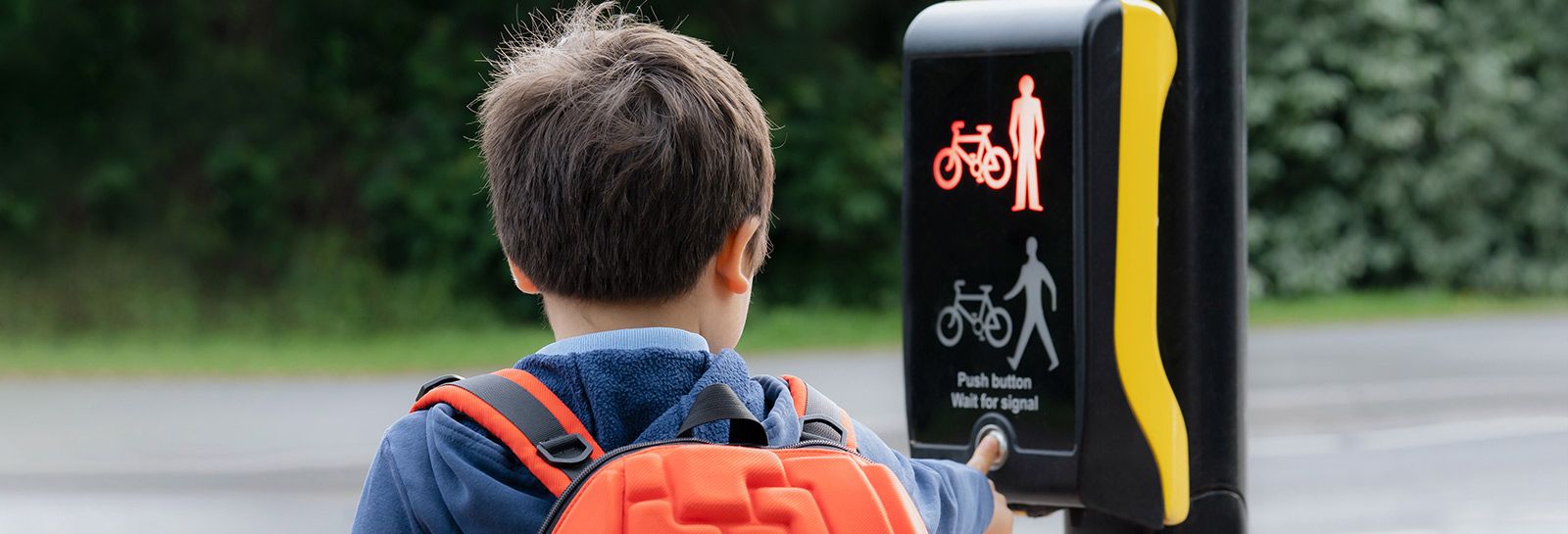 School boy waits at pedestrian crossing banner image